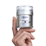 A hand holding a clear jar of Obagi Medical Elastiderm Lift-Up & Sculpt Facial Moisturizer against a solid white background.