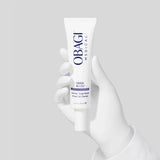 A white Obagi Medical serum tube held by a white gloved hand against a light gray background.