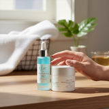 Elume Med Spa Ultra Hydrating Bundle with serum and moisture cream on a wooden table with a hand reaching for them.